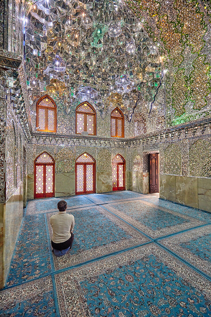 A man prays in the Ali Ibn Hamzeh Holy Shrine elaborately decorated inside with shiny mirror tiles (aina-kari). Shiraz, Iran.