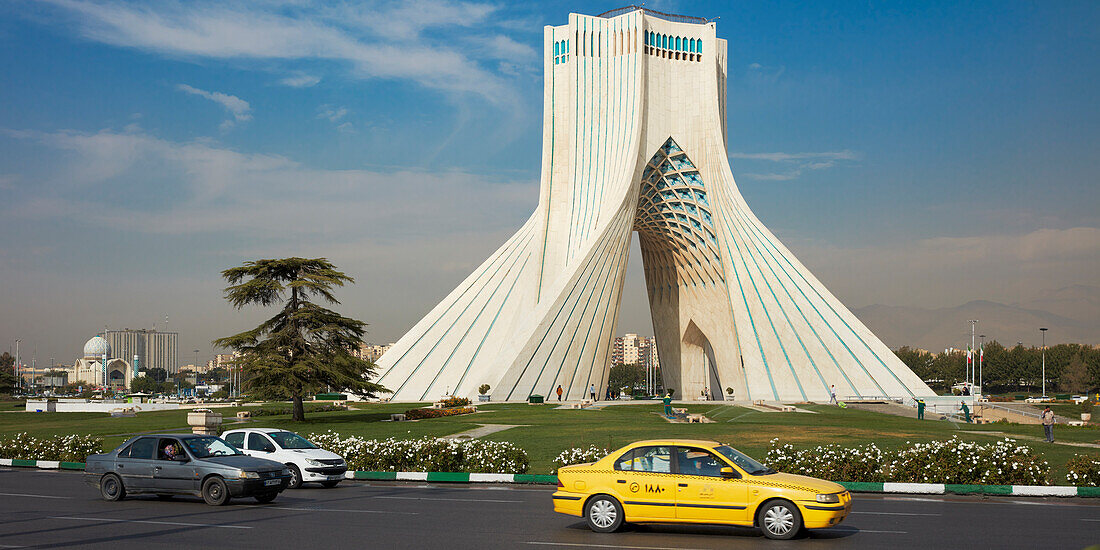 Yellow taxi passes by the Azadi Tower (Freedom Tower), an iconic landmark in Tehran, Iran.