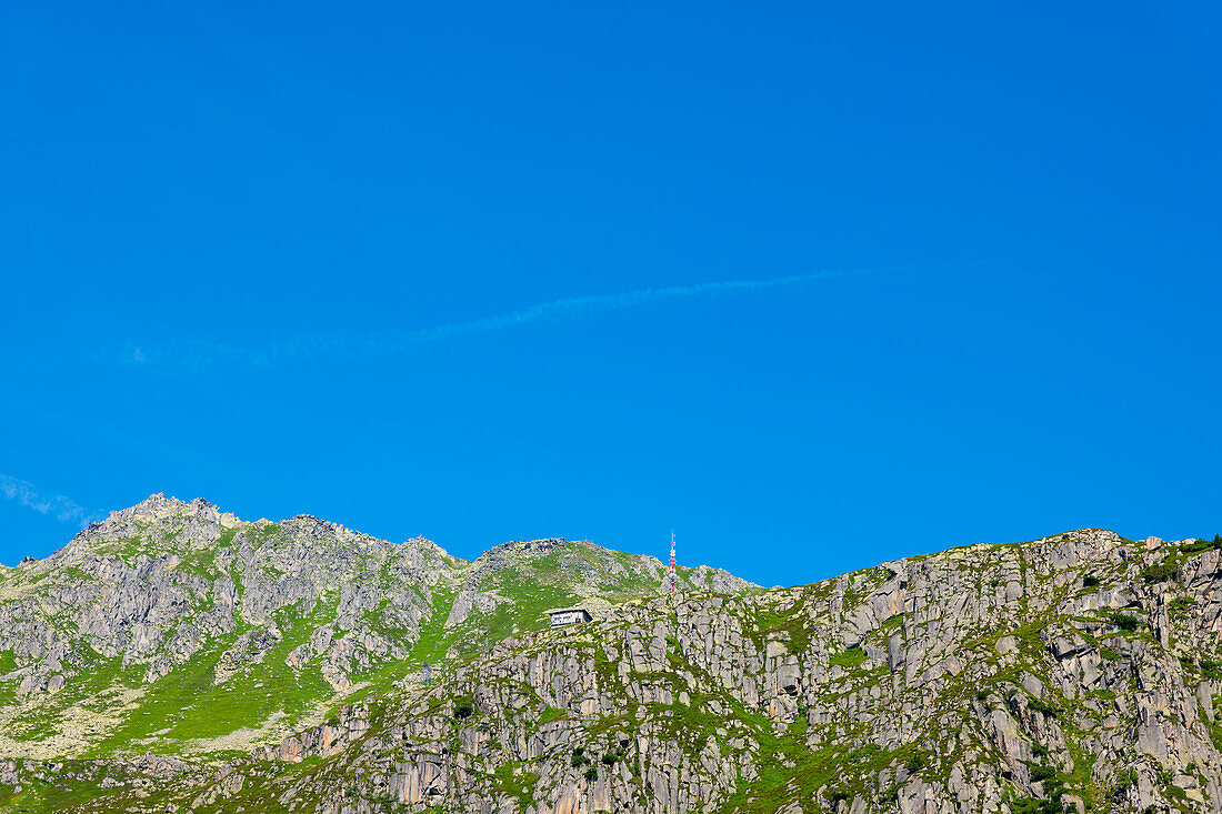 Haus und Kommunikationsturm auf einer Bergkette vor blauem Himmel an einem sonnigen Sommertag in Andermatt, Uri, Schweiz.