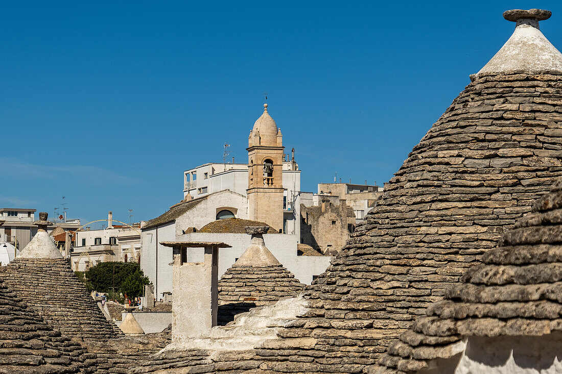  Trulli-Häuser mit der Kirche Santa Lucia im Hintergrund in Alberobello, Apulien, Italien. 