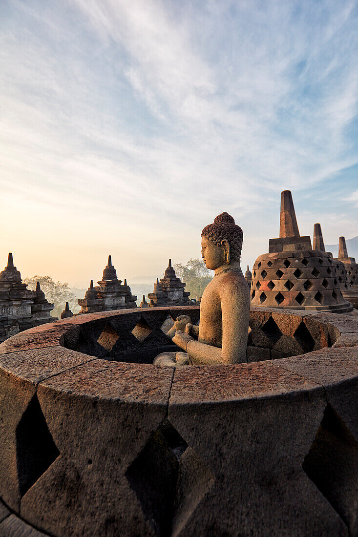 Buddha statue with the hand position of Dharmachakra mudra, representing Turning the Wheel of Dharma. Borobudur Buddhist Temple, Java, Indonesia.