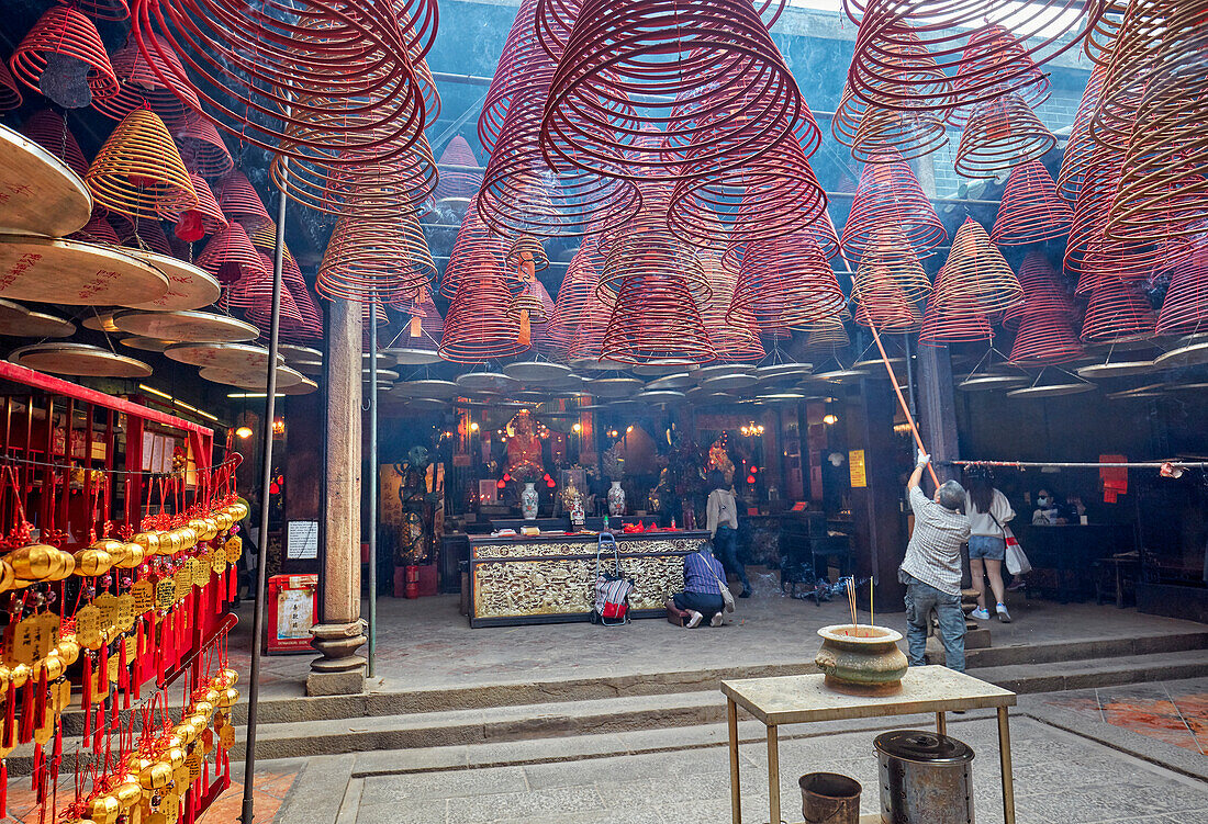 A man hangs up burning incense spirals in the Tin Hau Temple Complex. Yau Ma Tei, Kowloon, Hong Kong, China.