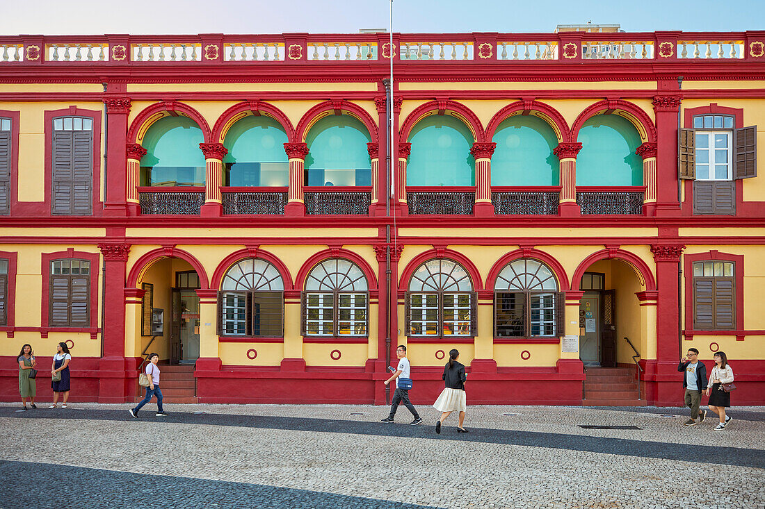  Menschen gehen am farbenfrohen Gebäude der Zentralbibliothek von Macau vorbei. Macau, China. 