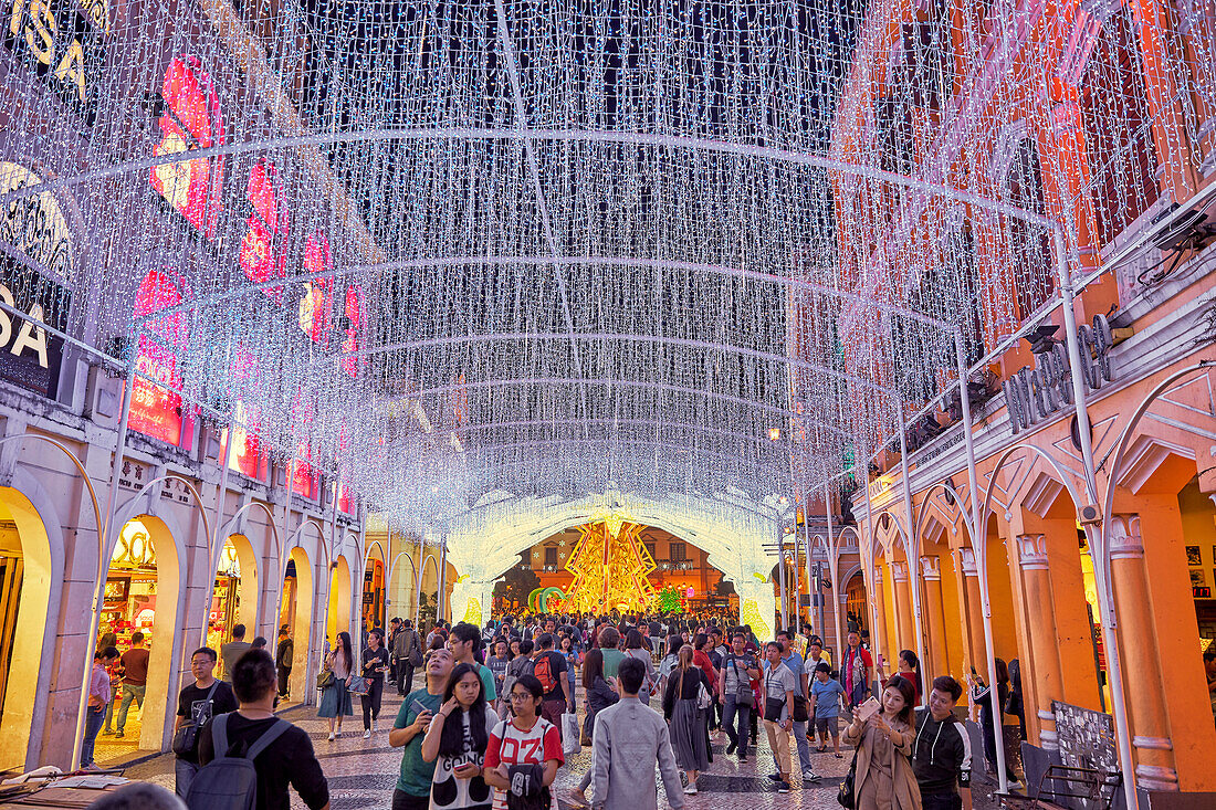 Crowd of people walking in historic Senado Square (Largo do Senado) brightly illuminated at night. Macau, China.