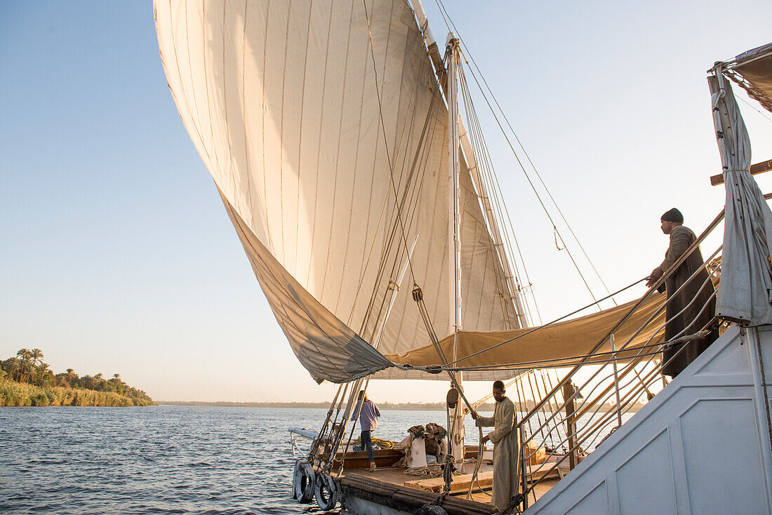 Einheimische auf Dahabeah Schiff unter Segeln, Passagier-Flussschiff der Lazuli-Flotte, auf dem Nil bei Sonnenuntergang, bei Assuan, Ägypten, Nordostafrika