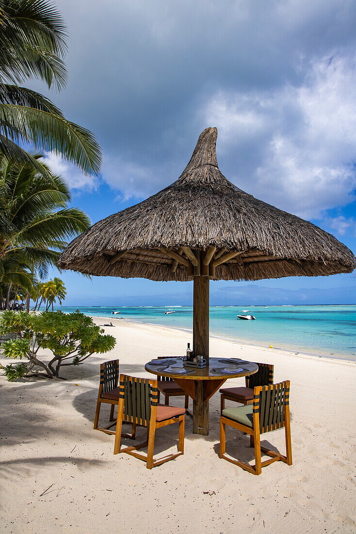 Tisch und Stühle mit Strohschirm am Strand im Paradis Beachcomber Golf Resort & Spa, Le Morne, Rivière Noire, Insel Mauritius, Indischer Ozean