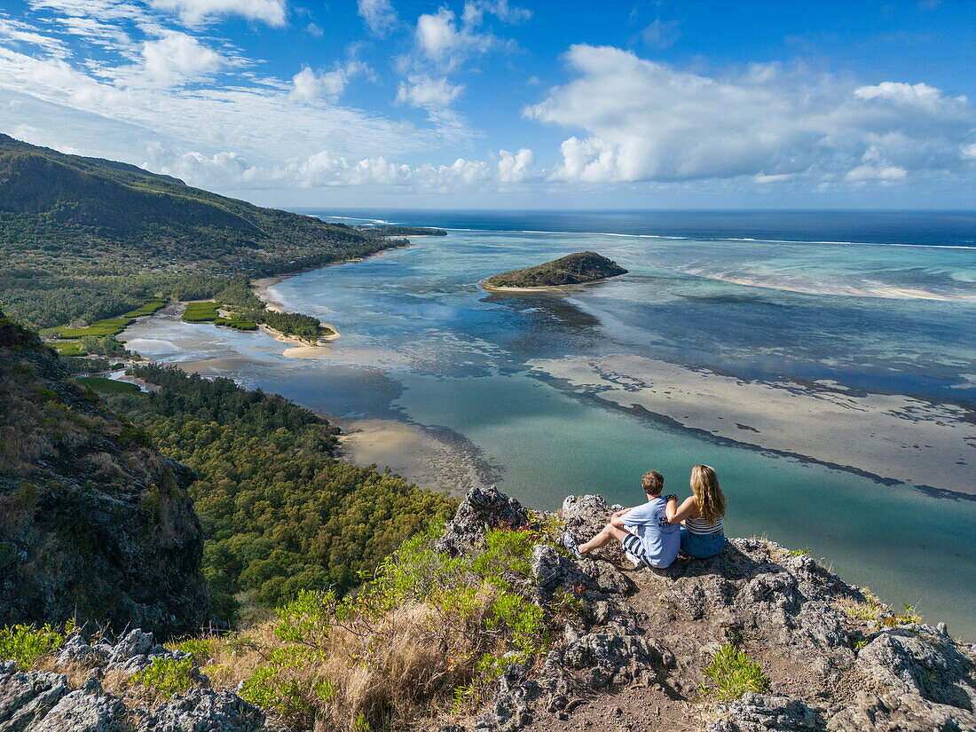  Aerial view of couple enjoying view over lagoon and coast halfway through hike up Le Morne mountain, Le Morne, Rivière Noire, Mauritius, Indian Ocean 