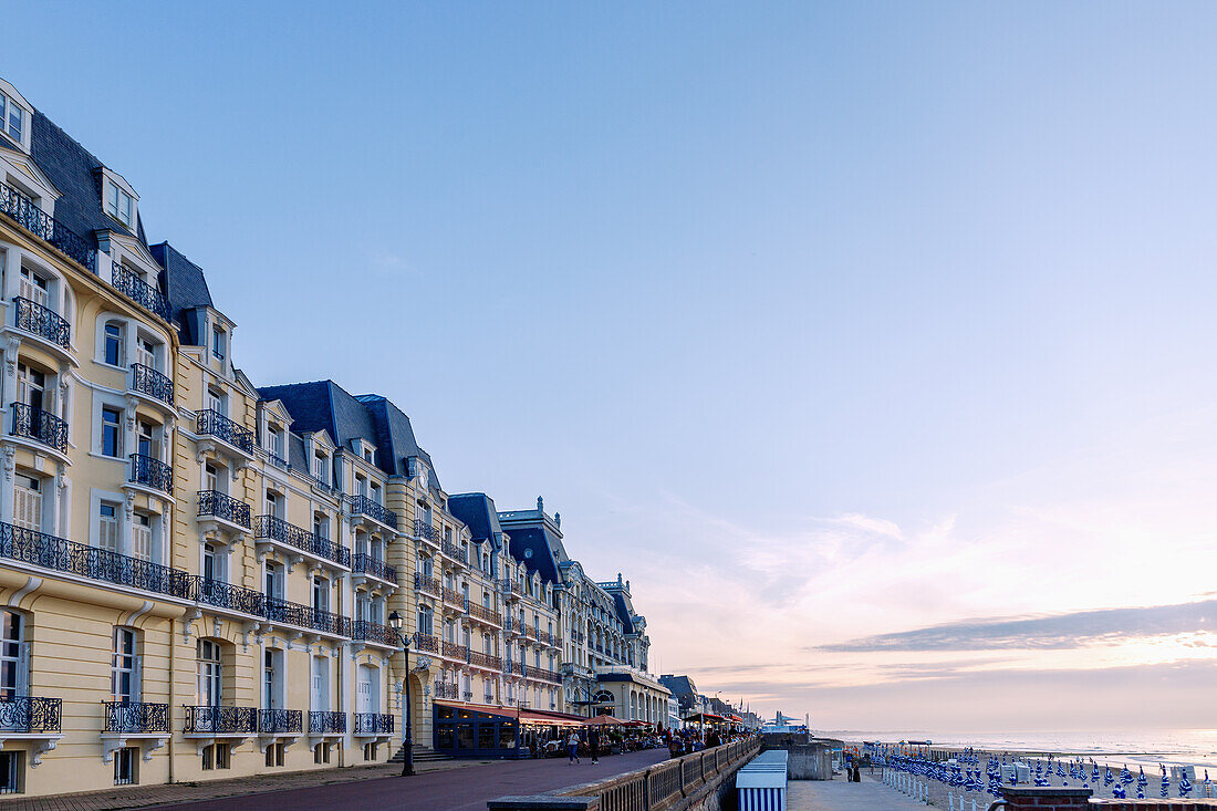  Beach promenade (Promenade Marcel Proust) with Grand Hotel (Le Grand Hôtel) and casino, bathing huts and folded umbrellas on the beach at sunset in the evening light in Cabourg on the Flower Coast (Côte Fleurie, Cote Fleurie) in the Calvados department in the Normandy region of France 