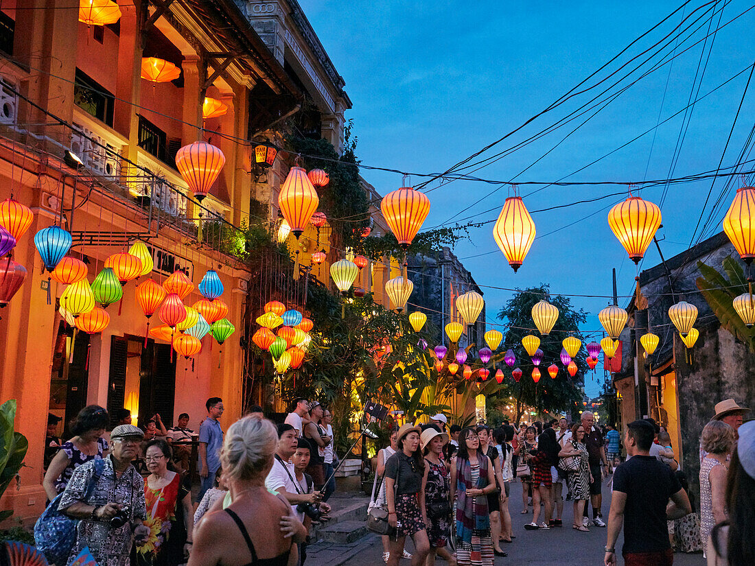 People walk in in Hoi An Ancient Town illuminated at dusk. Quang Nam Province, Vietnam.