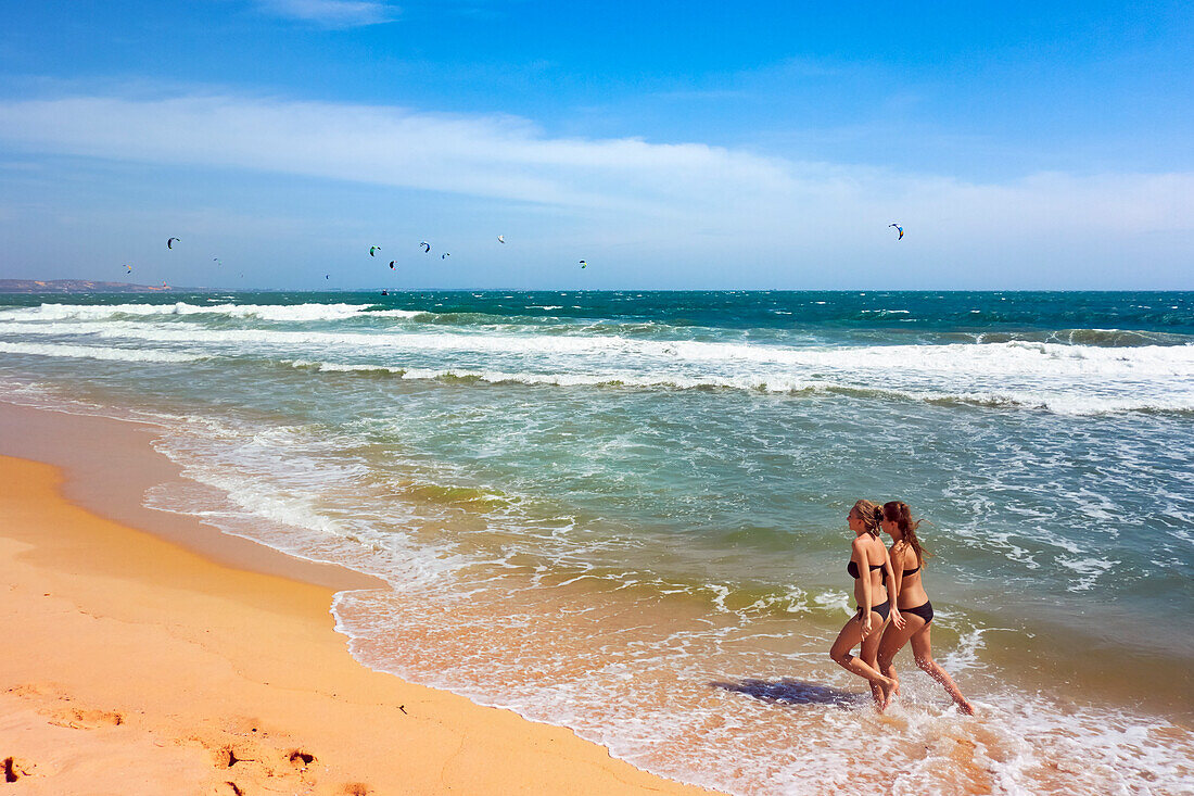  Zwei junge Frauen spazieren am Strand von Mui Ne entlang. Mui Ne, Provinz Binh Thuan, Vietnam. 