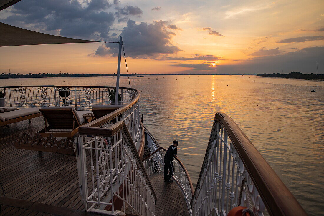 Matrose an der Reling des Boutique-Flusskreuzfahrtschiffs The Jahan (Heritage Line) auf dem Mekong bei Sonnenuntergang, Cai Lay, Tien Giang, Vietnam, Asien