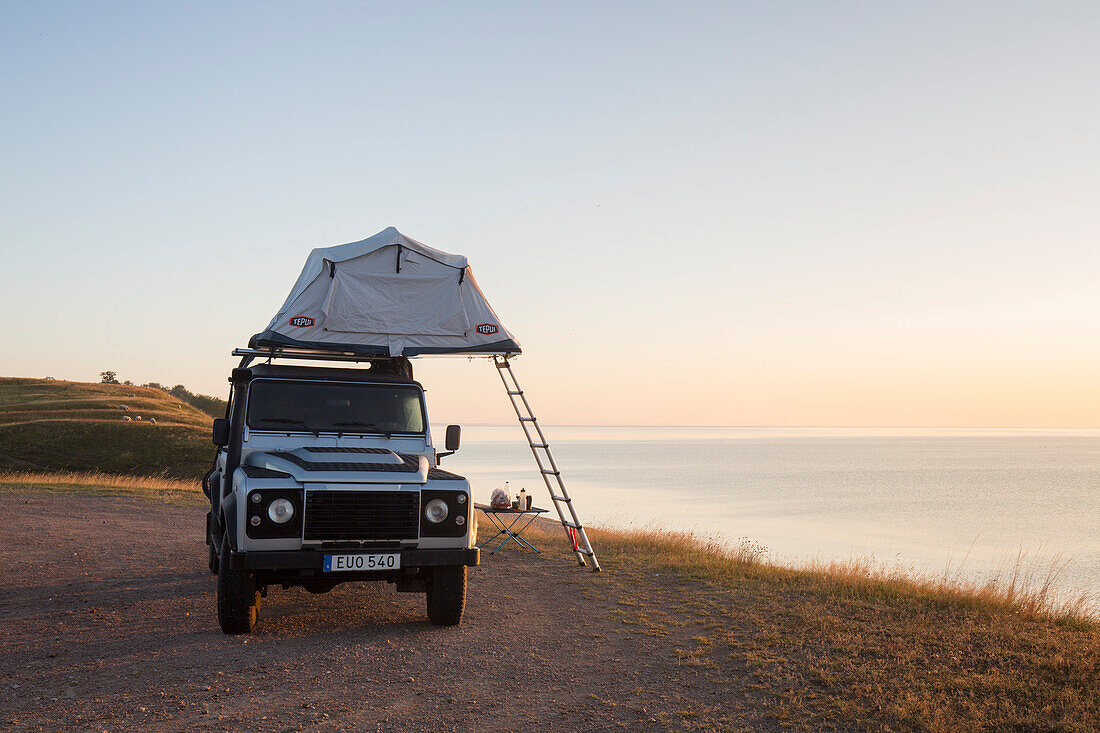  Off-road vehicle with roof tent camping at the Baltic Sea at sunrise, summer, Scania Province, Sweden 