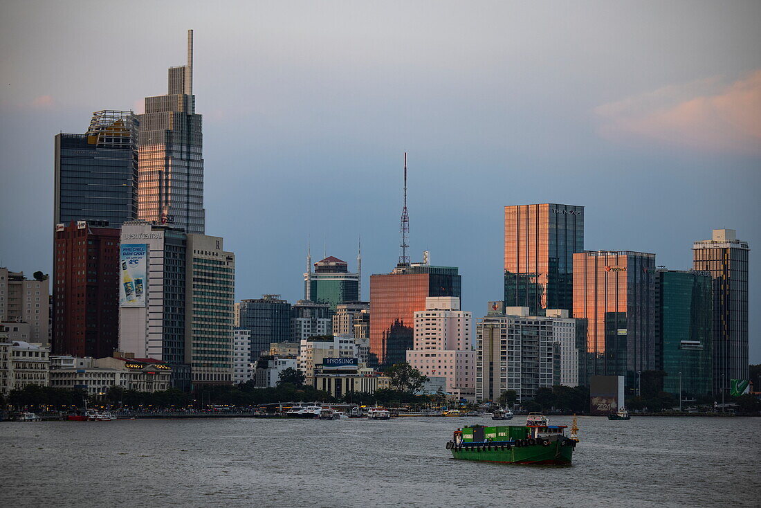 Frachtschiff auf dem Saigon-Fluss mit Skyline der Stadt bei Sonnenuntergang, Ho-Chi-Minh-Stadt, Vietnam, Asien