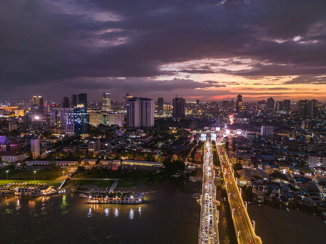  Aerial view of Chroy Changvar Bridge (also known as Cambodian-Japanese Kizuna Friendship Bridge) and river cruise ship RV Mekong Discovery anchored on Tonle Sap River with city skyline at dusk, Daun Penh District, Phnom Penh, Cambodia, Asia 