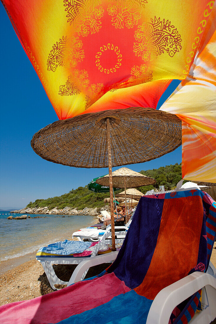 A lounge chair under parasol with a colorful canopy on a beach. Torba village, Bodrum peninsula, Turkey.