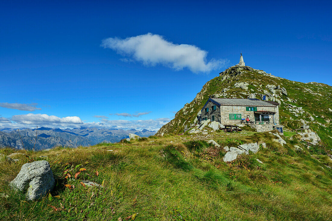 Frau sitzt vor Hütte Rifugio Mombarone mit Blick auf Gipfel Colma di Mombarone mit Christusstatue, GTA, Grande Traversée des Alpes, Biella, Alpi Biellesi, Walliser Alpen, Piemont, Italien