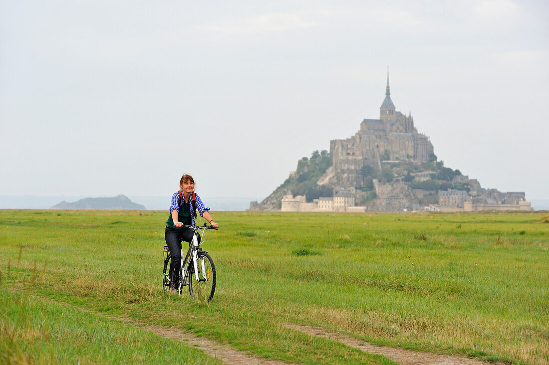 Junge Frau beim Radfahren vor Mont Saint-Michel, Département Manche, Region Basse-Normandie, Frankreich, Europa