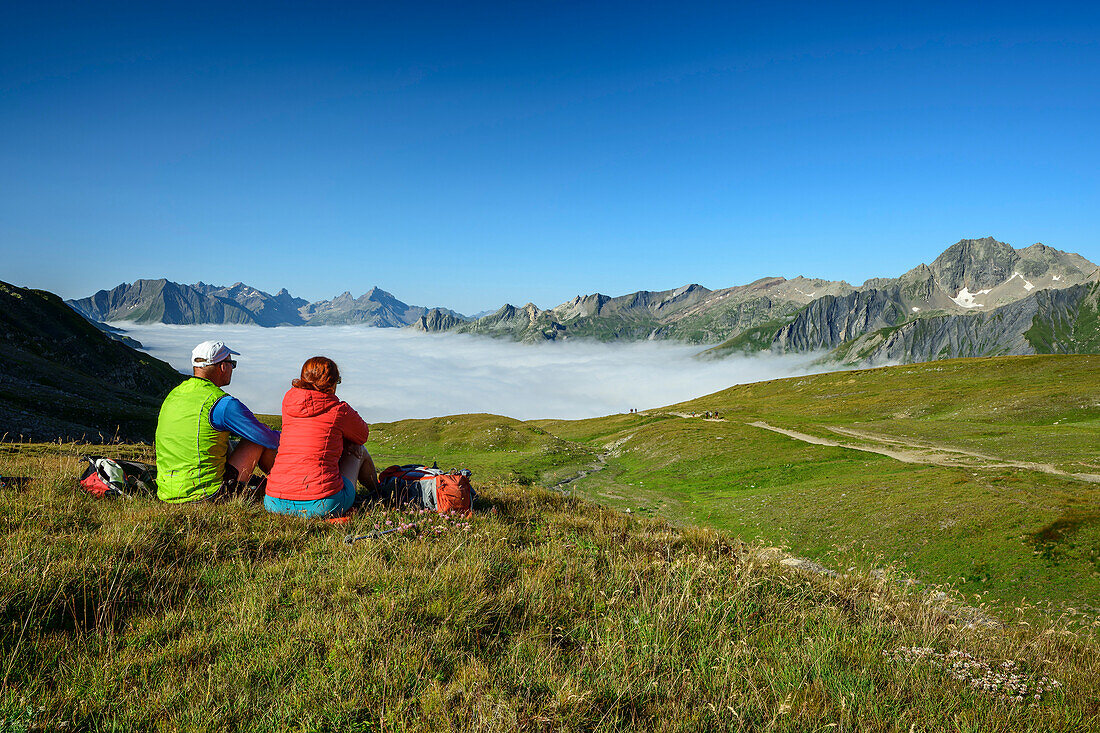  Man and woman hiking sitting at Col de la Seigne and looking at sea of fog, Col de la Seigne, Tour du Mont Blanc, Mont Blanc group, Graian Alps, Aosta Valley, Italy 