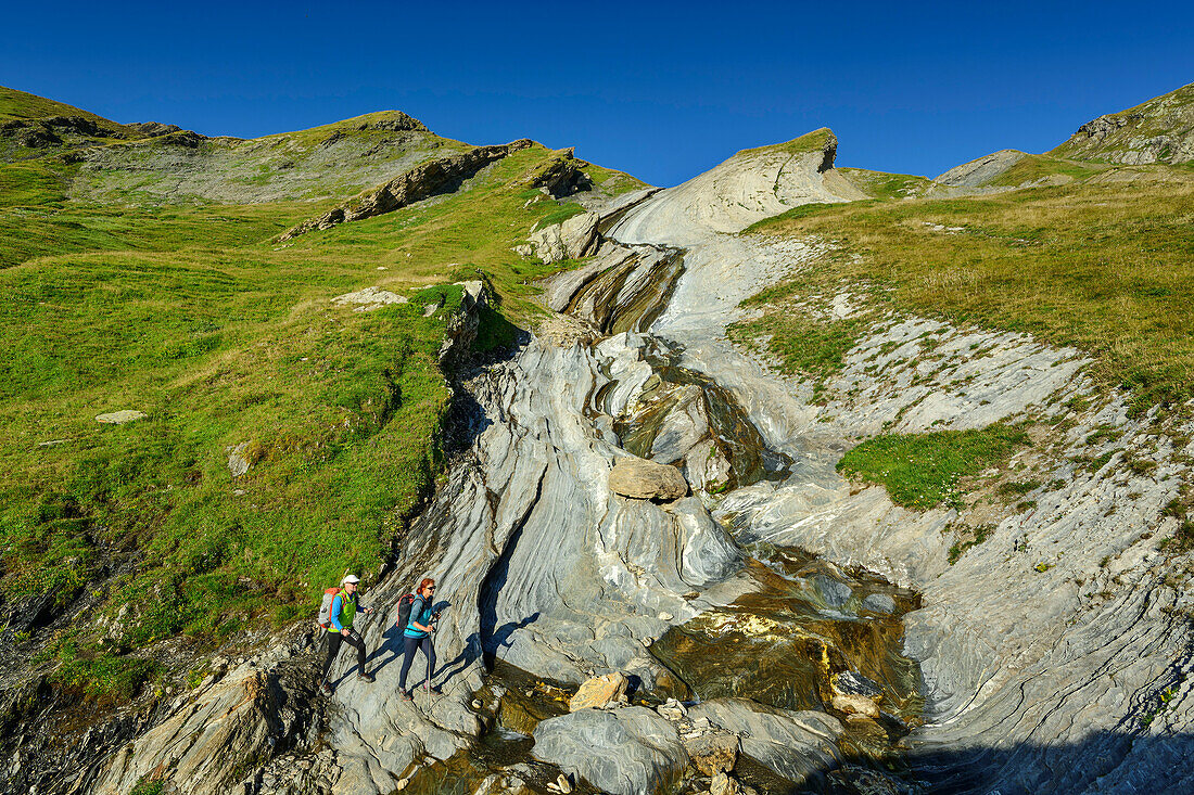 Mann und Frau beim Wandern überqueren Bach in Felsbett, am Col des Fours, Tour du Mont Blanc, Mont-Blanc-Gruppe, Grajische Alpen, Haute-Savoie, Hochsavoyen, Frankreich