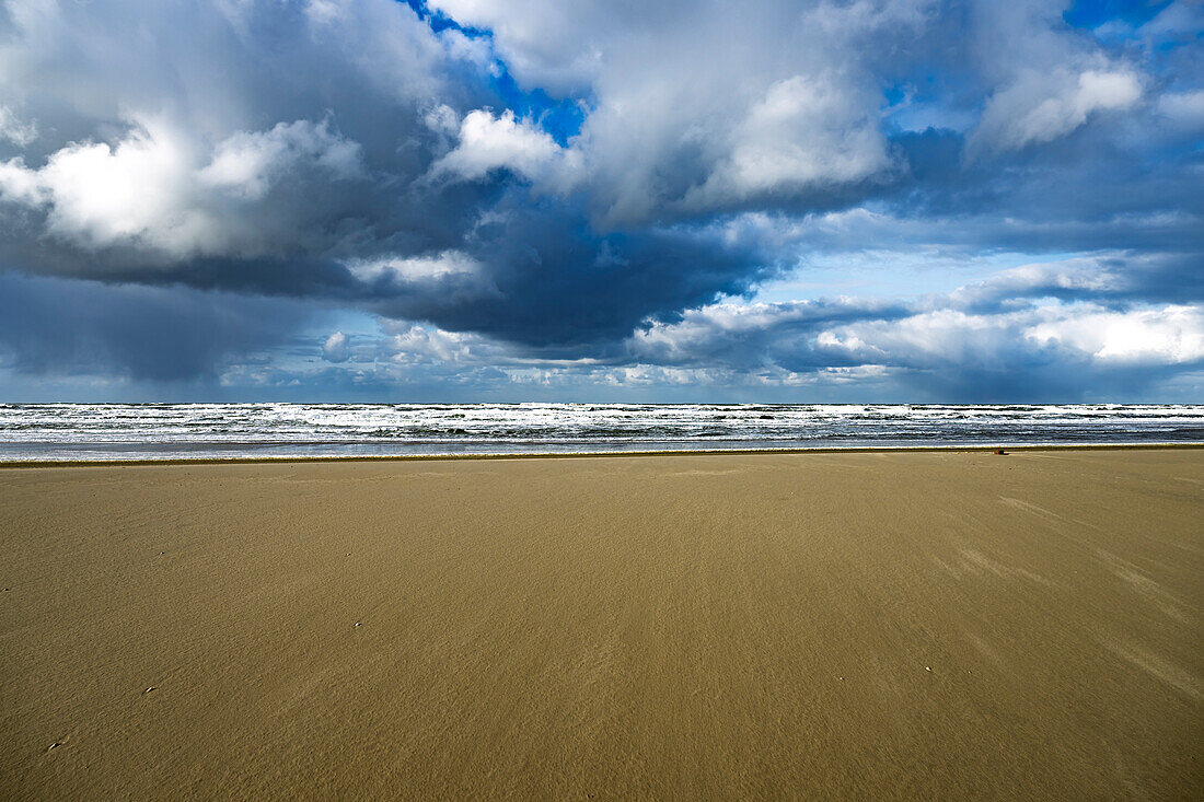 A vast sandy beach under a dramatic cloudy sky, with waves crashing in the distance.