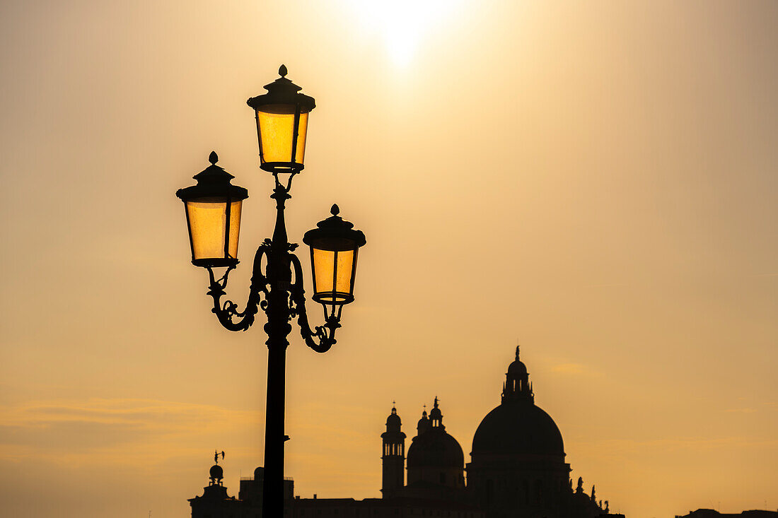 Laternenpfahl vor Silhouette der Basilica di Santa Maria della Salute vor goldenem Himmel, Venedig, Venetien, Italien