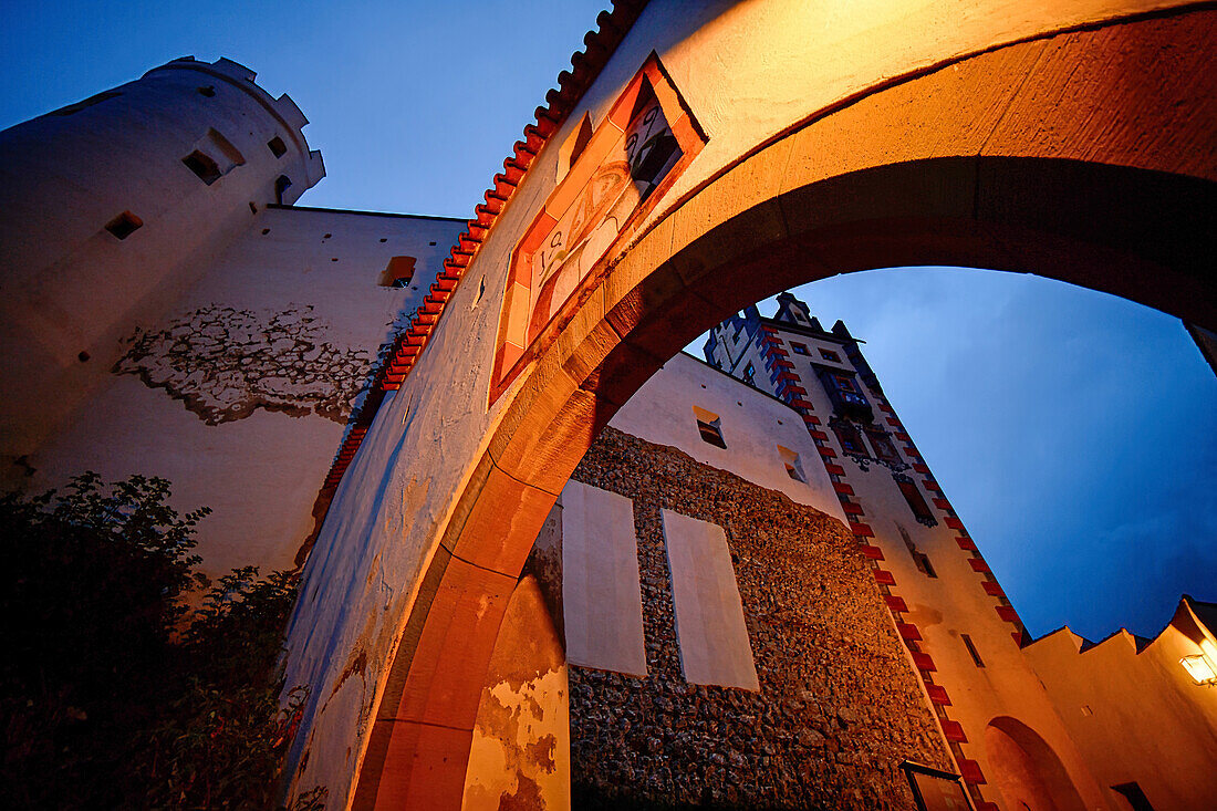  Stone archway and building of the High Castle in the old town of Füssen, illuminated in the evening, Bavaria, Germany 