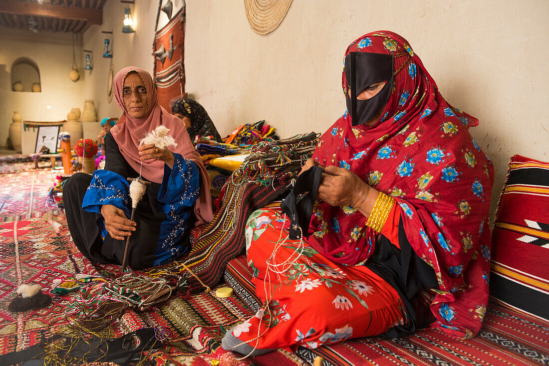 Two women, spinning and sewing, making a demonstration of his craft in the enclosure of the Fort of Nizwa, Ad Dakhiliyah Region, Sultanate of Oman, Arabian Peninsula, Middle East