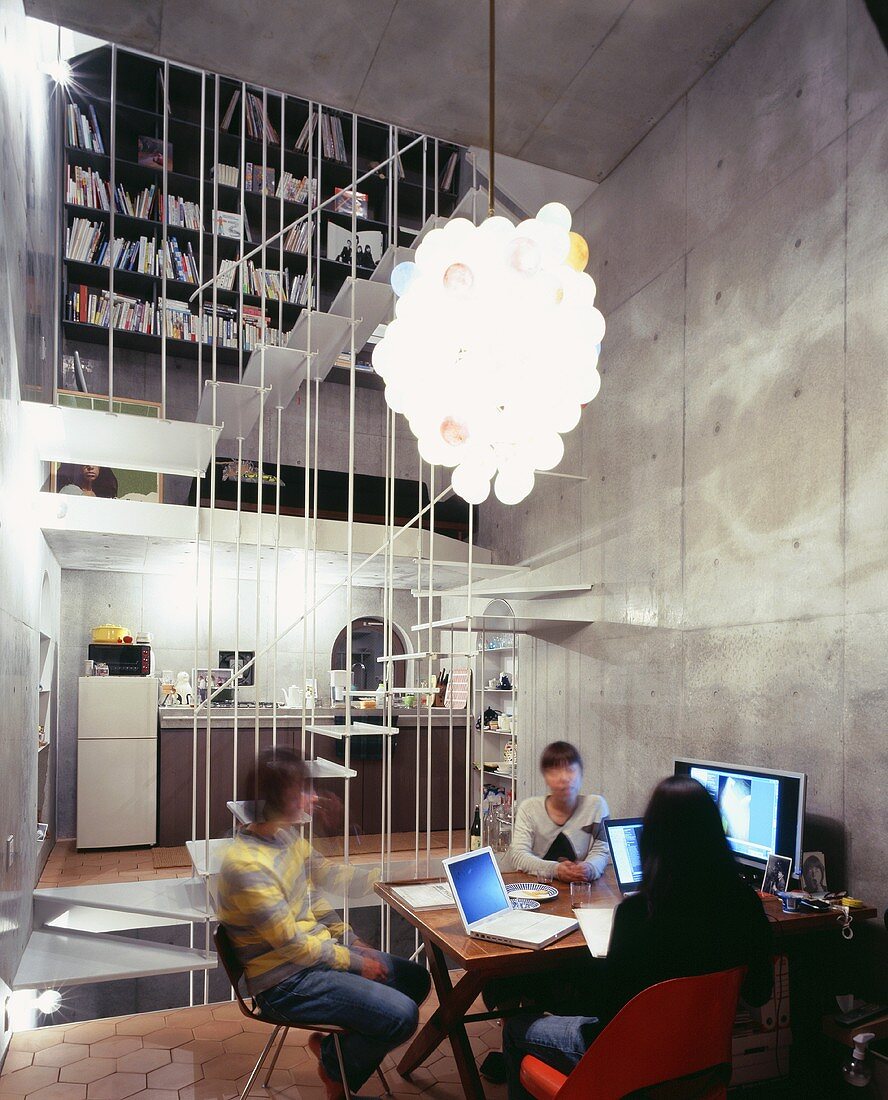 Young people sitting in front of a computer in an open-plan living room with an exposed concrete wall