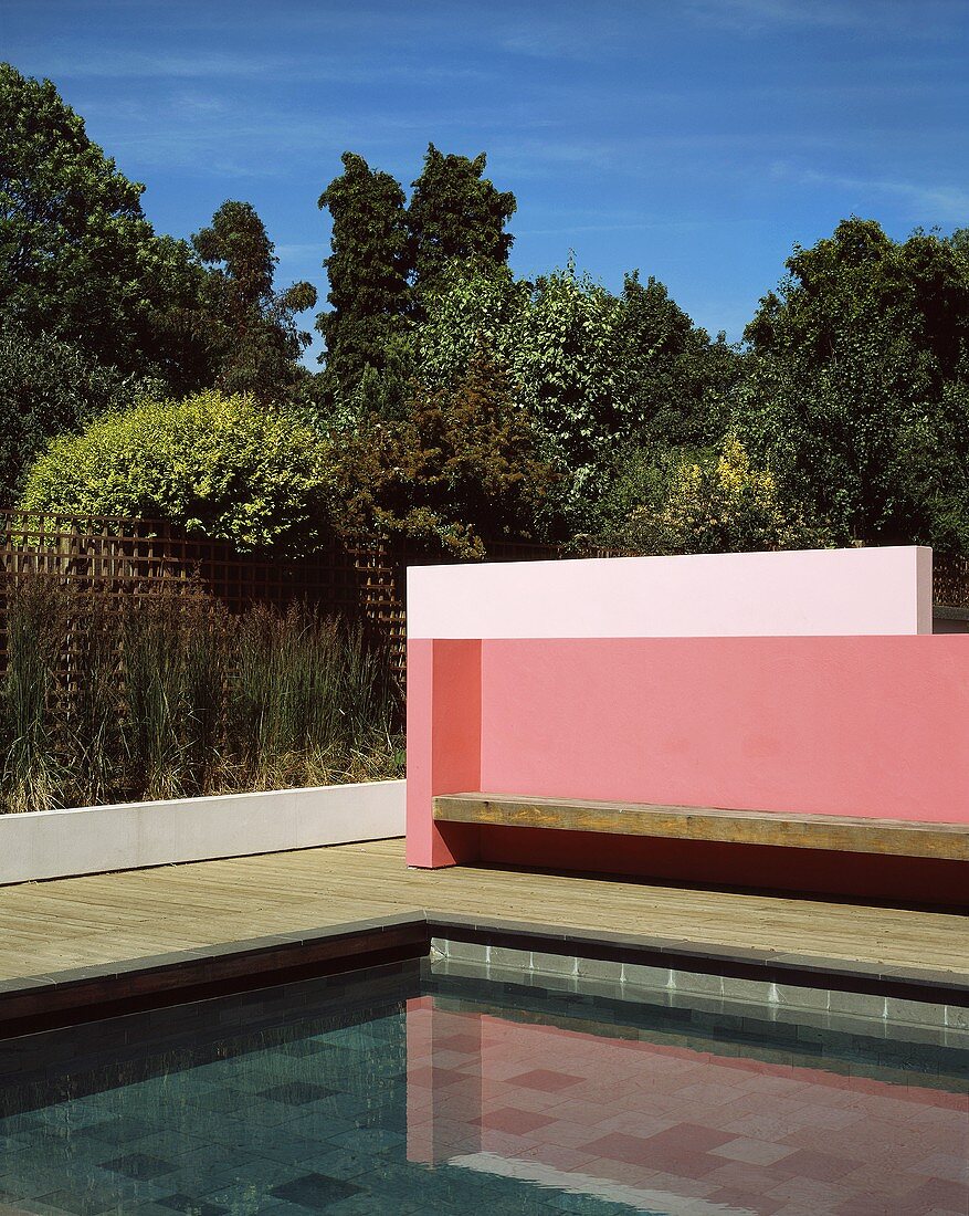 Corner detail of a modern pink-painted wall with a wooden bench in front of a pool