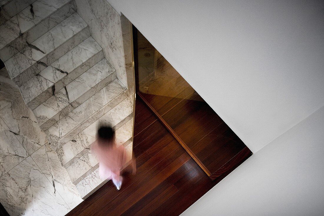 A view of a stairwell with marble steps in front of a red-brown wooden floor