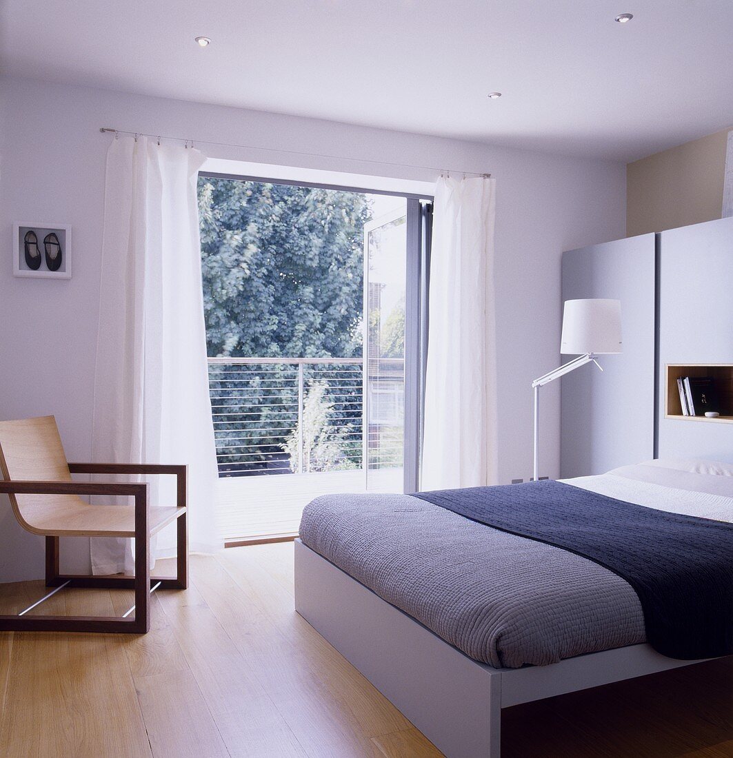 Modernes Schlafzimmer mit Doppelbett und Armlehnstuhl neben offenen Balkontüren