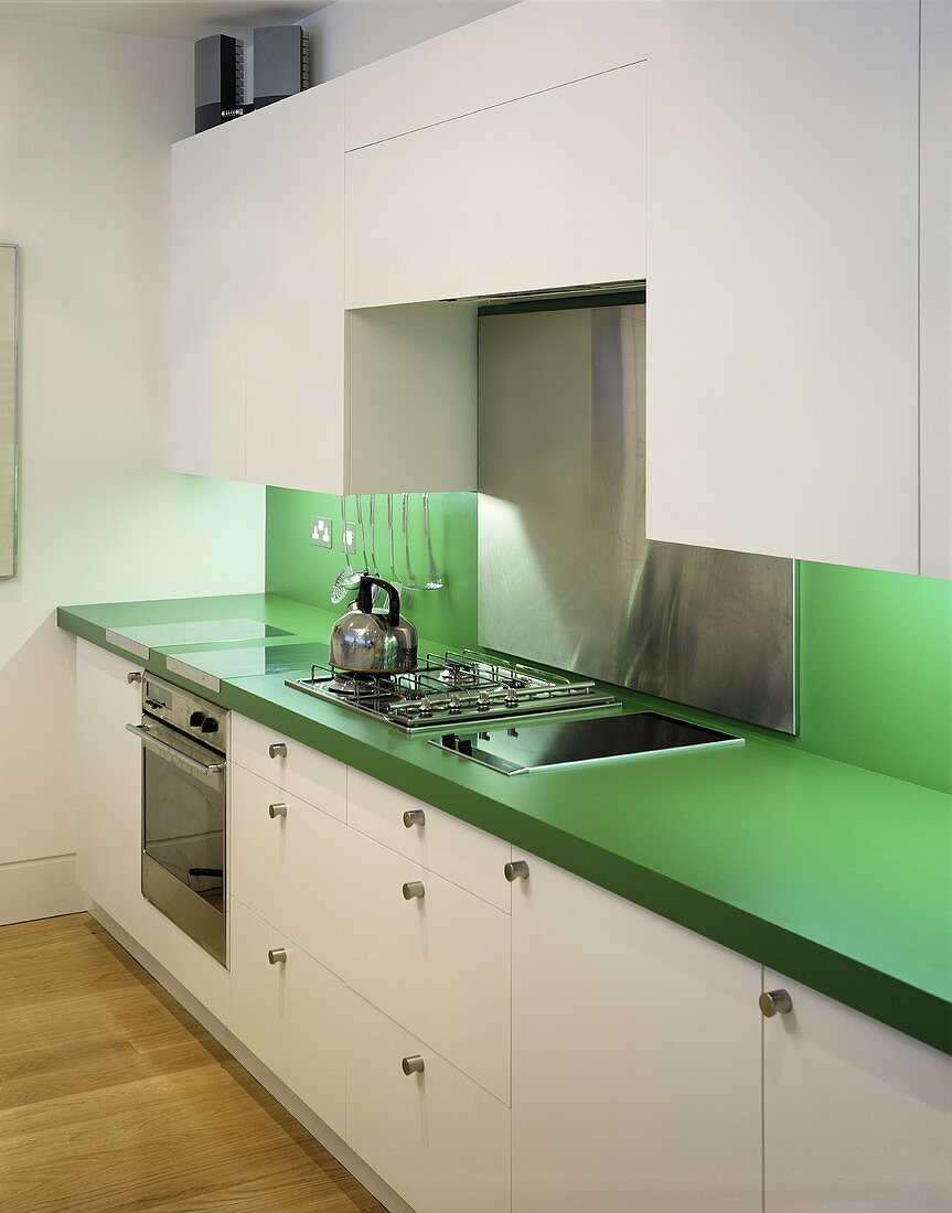 A white kitchen with a green work surface and a splash guard