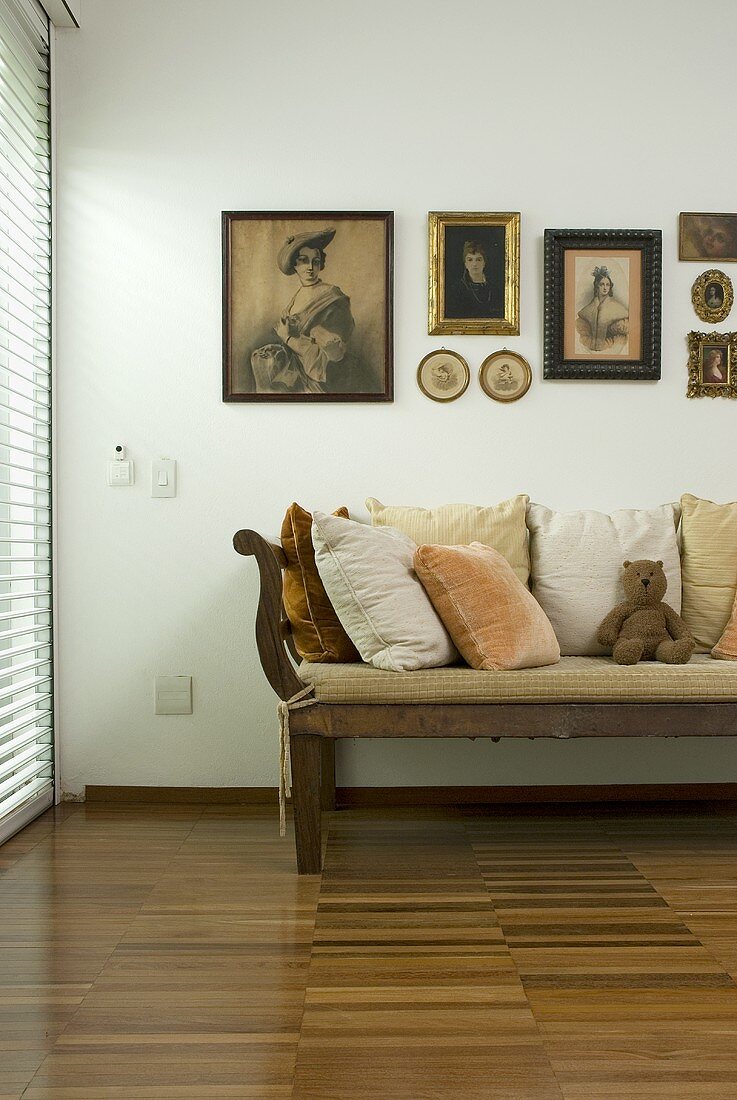 An antique bench and a collection of pictures on the wall in a room with a parquet floor