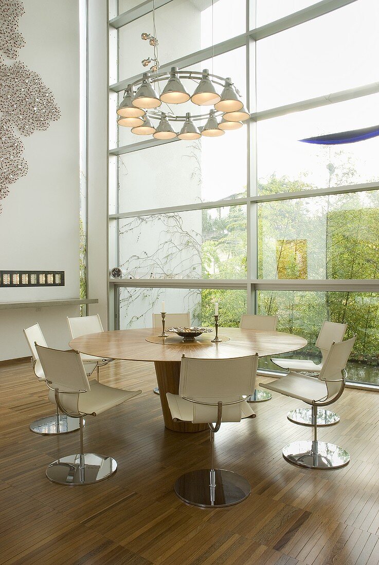 A designer lamp above a dining table with white swivel chair in front of a glass facade