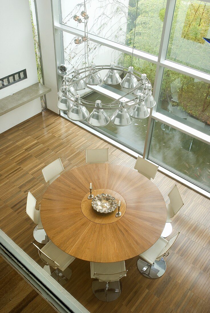 Aufsicht auf runden Tisch aus Holz und weissen Stühlen vor Glasfront im modernen Wohnraum