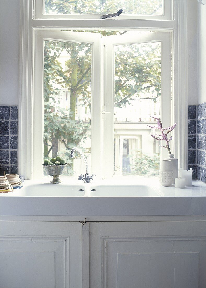 An antique porcelain sink under the window with a white cupboard underneath