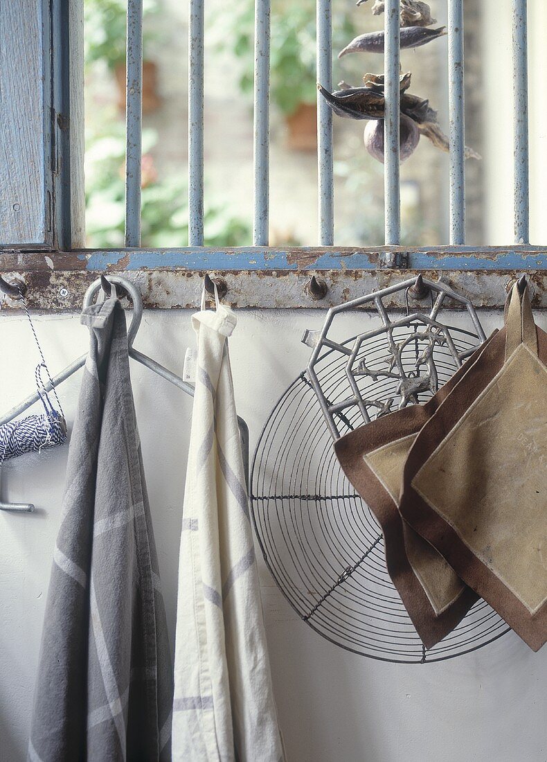 Tea towels, pan holders and other kitchen utensils hanging from a rusty bar with hooks