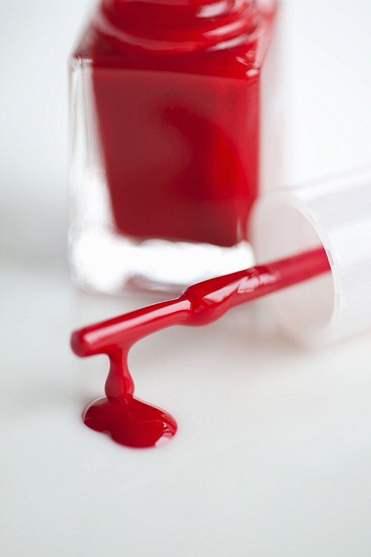 Red nail varnish, an open bottle and a dripping brush