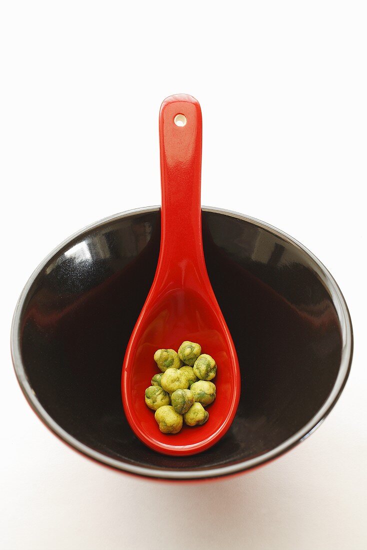 Wasabi peas on red spoon in lacquer bowl