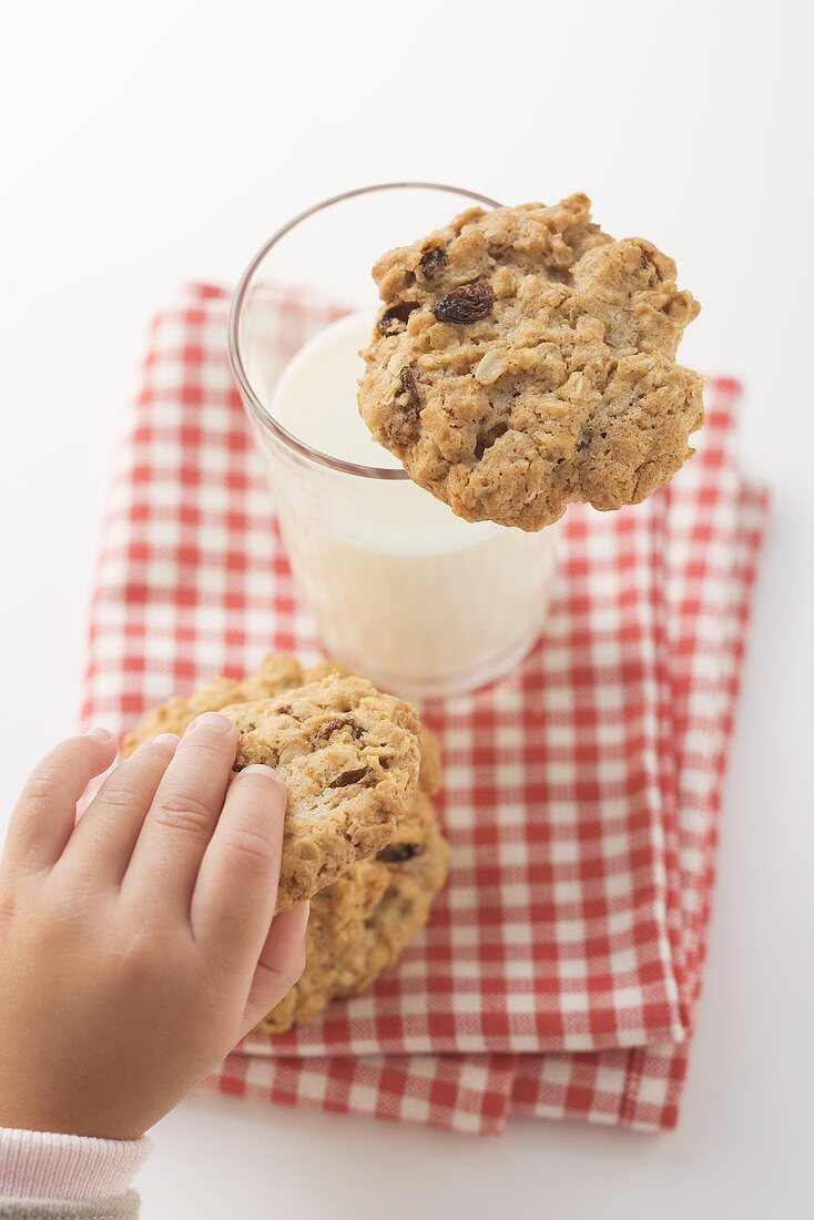 Child's hand reaching for cookie beside glass of milk