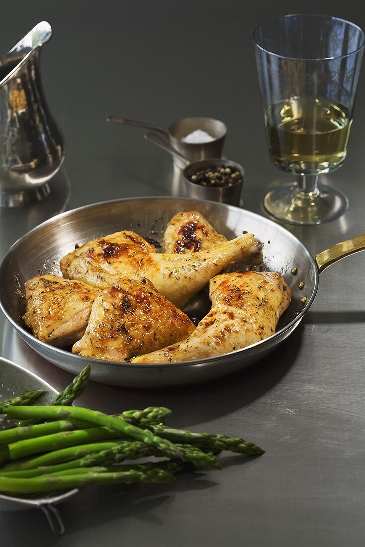 Fried chicken legs in a frying pan with asparagus