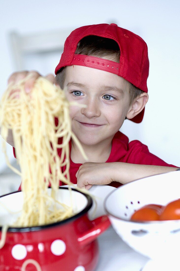 Kleiner Junge nimmt Spaghetti aus dem Kochtopf