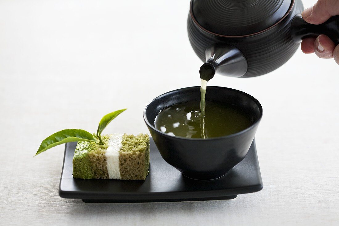 Grünen Tee wird eingeschenkt, daneben ein Stück Teekuchen