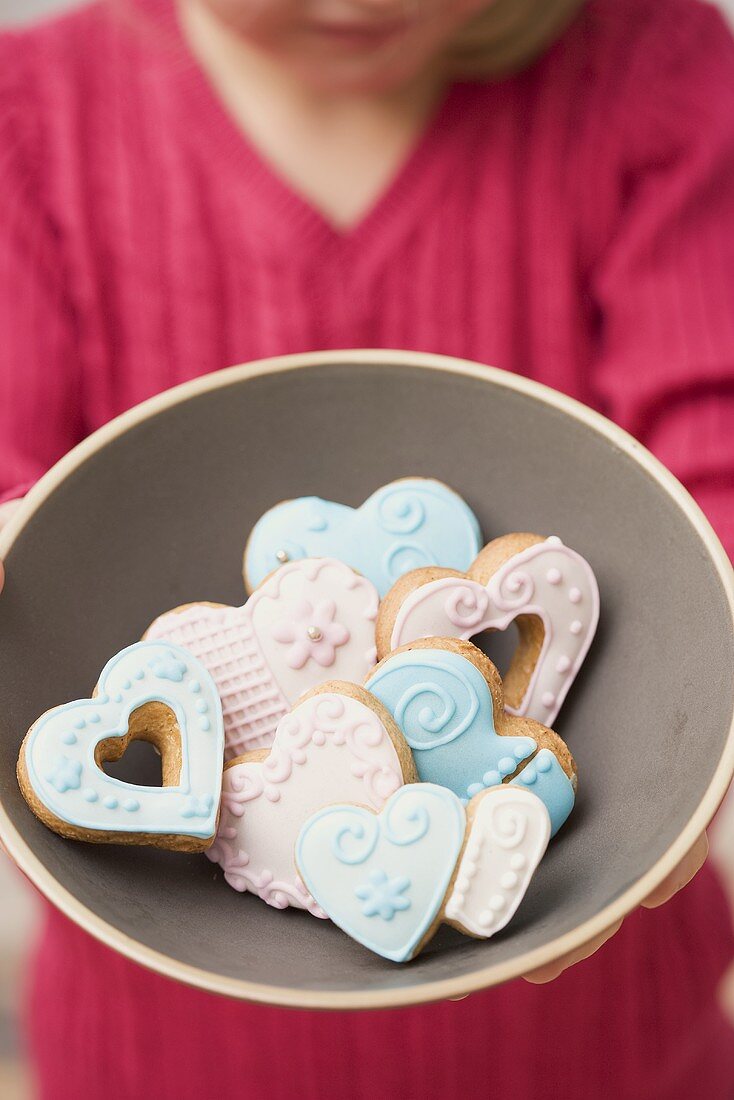 A girl holding a bowl of heart-shaped biscuits