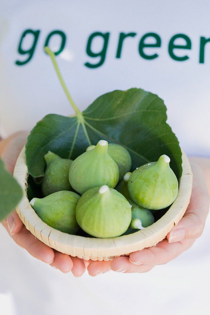 A woman holding a wicker bowl of fresh figs and leaves