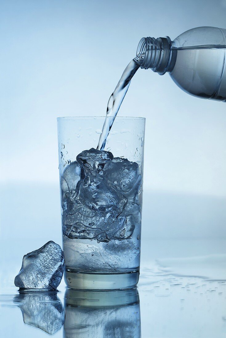 Wasser aus Flasche in Glas mit Eiswürfeln gießen