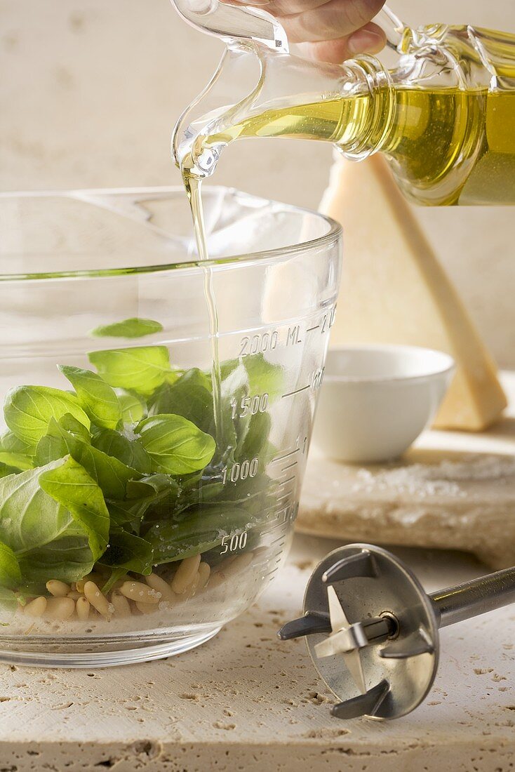 Pouring olive oil on basil leaves and pine nuts