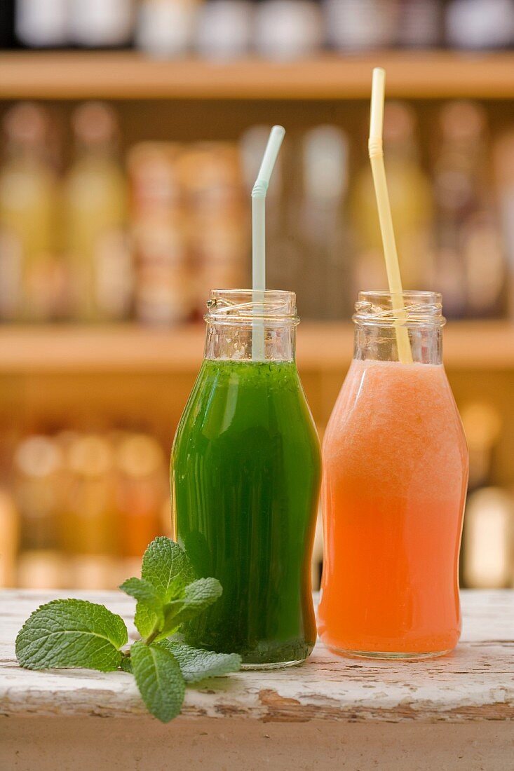 A cucumber smoothie and a melon smoothie in bottles with straws