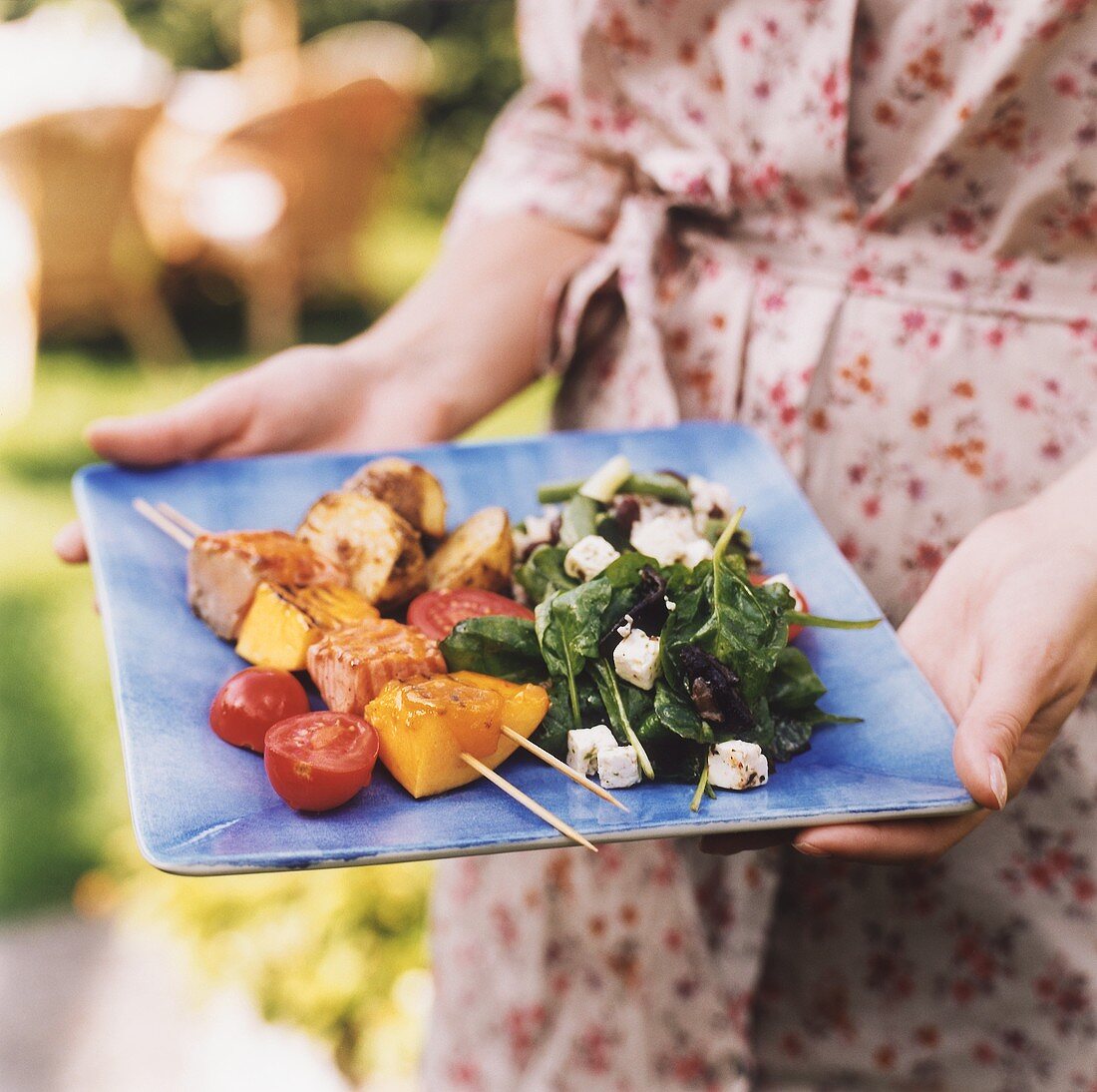 Frau hält einen Teller mit Gegrilltem und Salat