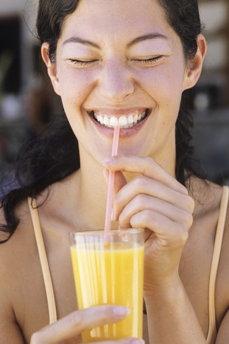 Junge Frau trinkt Orangensaft mit Strohhalm